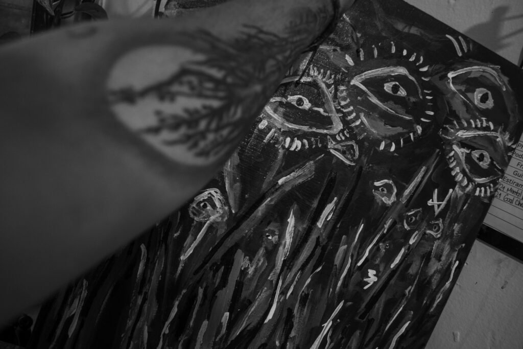 "THE WHISPER OF THE IDEA": A black and white close-up of a dark, textured painting, showing multiple abstract, elongated eyes that appear to be glowing or awakening.