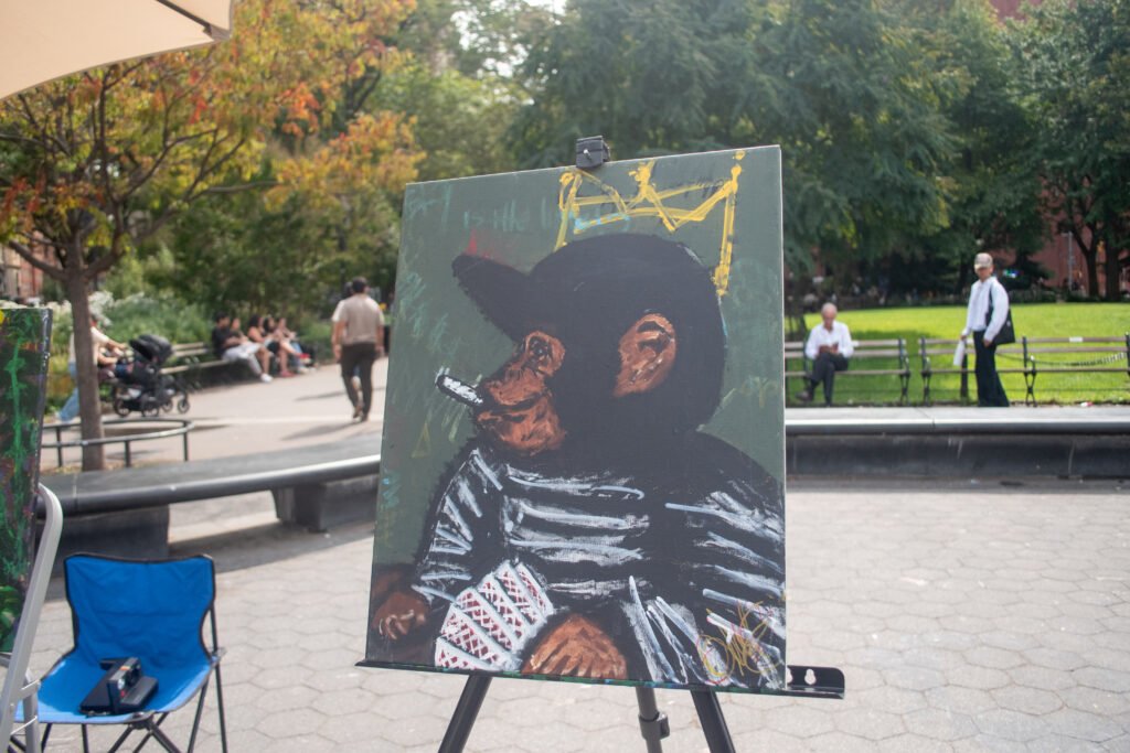 Painting on Easel: A painting on an easel in a park setting, featuring a black and white portrait of a chimpanzee or monkey-like figure smoking a pipe, wearing a baseball cap and striped clothing.Super Chango