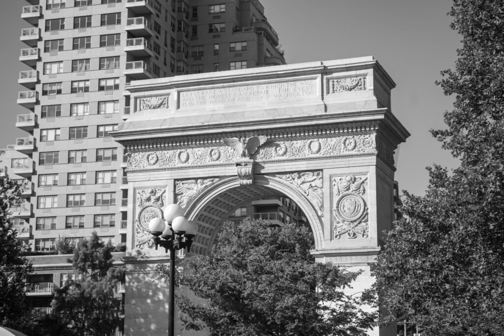 A black and white mid-shot of the Washington Square Arch in New York City, cropped to show the detailed stone carvings and reliefs. The word "KAIZEN" is overlaid across the center of the arch in white text.